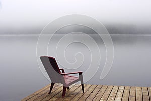 An Adirondack chair on wooden deck on lake in fog with copy space
