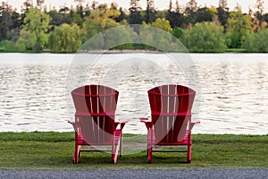 Adirondack red wooden chairs by lake shore. Peacefull scene.