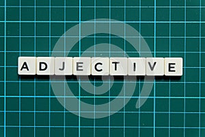 Adjective word made of square letter word on green square mat background.