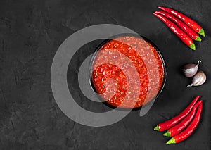 Adjika on a black background. Harissa sauce in a bowl with hot chili peppers. View from above. Space for text