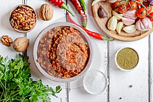 Adjika in a bowl and ingredients on a white wooden table.