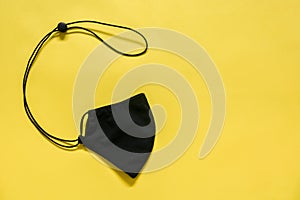 The adjustable black color folded protective cloth mask isotated on yellow background, copy space, flat lay