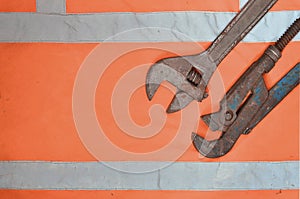 Adjustable and pipe wrenches against the background of an orange signal worker shirt. Still life associated with repair, railway