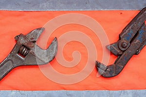 Adjustable and pipe wrenches against the background of an orange signal worker shirt. Still life associated with repair, railway