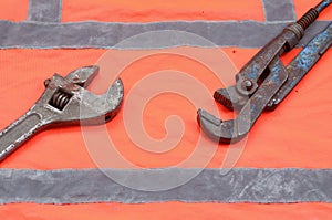 Adjustable and pipe wrenches against the background of an orange signal worker shirt. Still life associated with repair, railway
