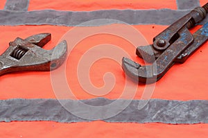 Adjustable and pipe wrenches against the background of an orange signal worker shirt. Still life associated with repair, railway