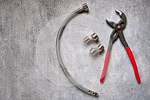 Adjustable pliers, plumbing eccentrics and flexible connection hose on gray concrete background close-up