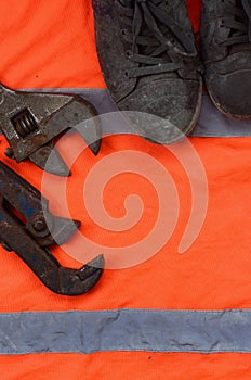 Adjustable wrenches and old boots lies on an orange signal worker shirt
