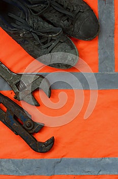 Adjustable wrenches and old boots lies on an orange signal worker shirt