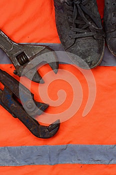 Adjustable wrenches and old boots lies on an orange signal worker shirt