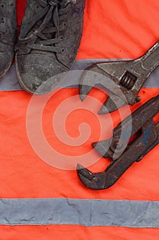 Adjustable wrenches and old boots lies on an orange signal worker shirt. Still life associated with repair, railway or plumbing w