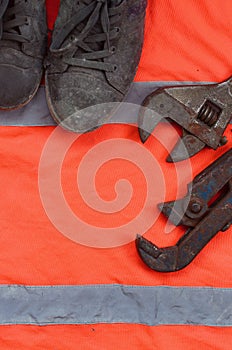 Adjustable wrenches and old boots lies on an orange signal worker shirt. Still life associated with repair, railway or plumbing w