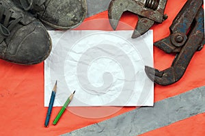 Adjustable wrenches with old boots and a sheet of paper with two pencils. Still life associated with repair, railway or plumbing