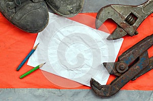 Adjustable wrenches with old boots and a sheet of paper with two pencils. Still life associated with repair, railway or plumbing