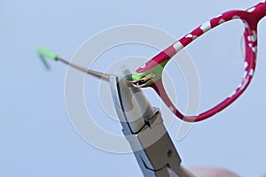 Adjusting inclination on patchy red and white children eyeglass frame with conical nylon jaws inclination pliers.