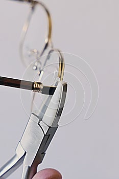 Adjusting inclination of temples on modern metal eyeglass frame with conical inclination pliers photo