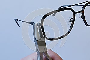 Adjusting inclination of temples on modern plastic and metal eyeglass frame with conical inclination pliers photo