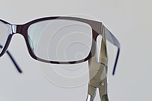 Adjusting inclination of temples on simple plastic eyeglass frame with steel chain nose pliers. photo