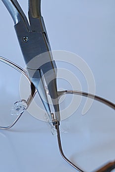Adjusting nose pad position on metal eyeglass frame with flat snipe nose pliers.