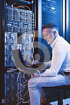 Administering all systems. a mature man using a laptop while working in a server room.