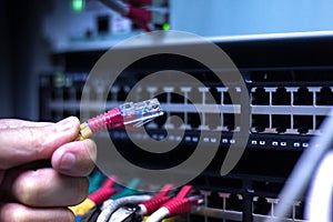 Administrator Hand with network cables connected to servers in datacenter photo