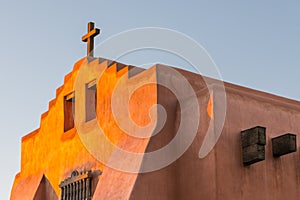 Adobe church and rustic wooden cross glow in golden evening light in Santa Fe, New Mexico