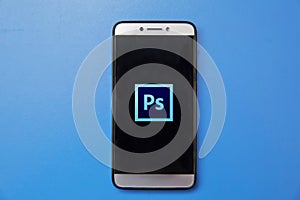 Adobe Photoshop logo on smartphone screen on blue background. Man holding smartphone with Adobe photoshop logo on the screen.