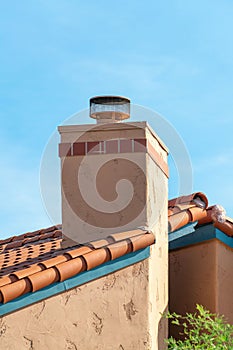 Adobe style chimney on a ranch style home or house with cream or beige cement exterior and visible metal vents in yard