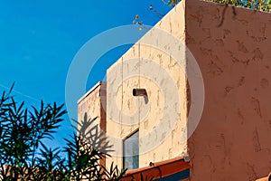 Adobe style orange cement building with front or back yard trees with clear blue sky background in neighborhood