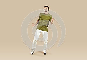 Adolescent boy dancing and singing in headphones enjoying music on beige background in studio.