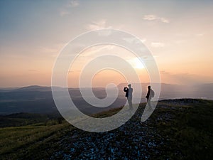 Adolescent boy taking photos of a sunset in the company of a girl with backpack