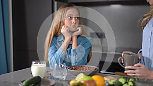 Adolescent Caucasian female teenager talking to young unrecognizable woman in kitchen at home. Medium shot portrait of