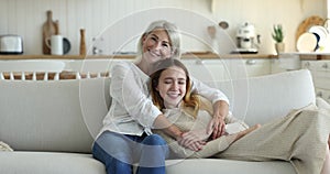 Adolescent daughter resting on couch with middle-aged attractive mother
