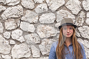 Adolescent girl in a hat and denim jacket against a white stone walls. Walk.