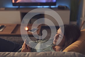 Adolescent girl lying down on the couch and connecting with her smartphone