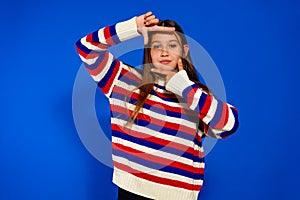 Adolescent girl in a striped sweater making the gesture of being framed by a camera. She practices to be an actress when