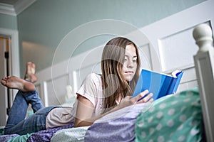 Adolescent teen girl reading a book while lying in bed at home in her bedroom. Lifestyle and learning photo