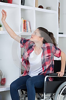 Adolescent in wheelchair reaching up to shelf