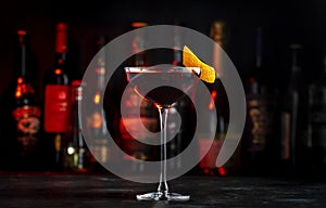 Adonis alcoholic cocktail drink with sherry and red vermouth, black bar counter background, steel tools and bottles