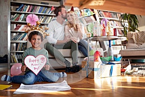 An adopted little boy with a present he made for his mother is posing for a photo at a kids birthday party at home with his family photo