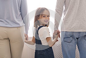 Little Girl Holding Hands With Unrecognizable Man And Woman And Smiling photo