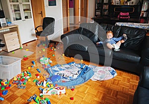 Adorable 1 year old baby boy with funny facial expression playing in a very messy living room