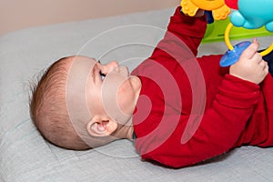 Adorable 6 months old little baby boy on his back surrounded by colourful toys