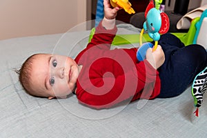 Adorable 6 months old little baby boy on his back surrounded by colourful toys