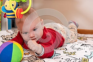 Adorable 6 months old little baby boy during tummy time surrounded by colourful toys