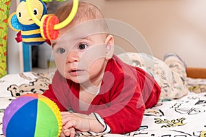 Adorable 6 months old little baby boy during tummy time surrounded by colourful toys