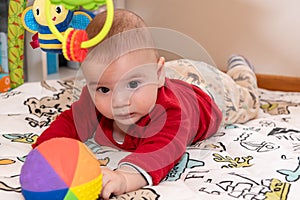 Adorable 6 months old little baby boy during tummy time surrounded by colourful toys