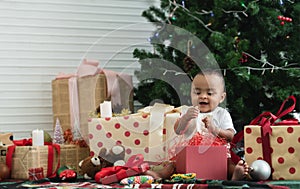 Adorable 9 months African baby smiling and having fun to open gift box, sitting in front of Christmas tree on floor