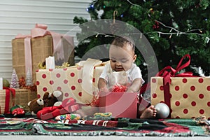 Adorable 9 months African baby smiling and having fun to open gift box, sitting in front of Christmas tree on floor