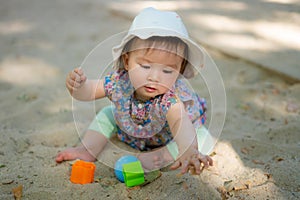 Adorable 9 months old baby playing outdoors - lifestyle portrait of mixed ethnicity Asian Caucasian baby girl playing with block